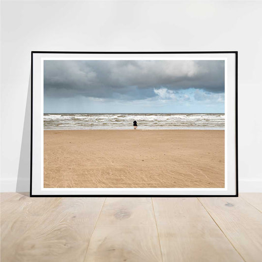 This photograph of a lone woman standing on an empty beach with her back to the camera, facing a receding tide under large, dark clouds, evokes a profound sense of solitude and introspection.