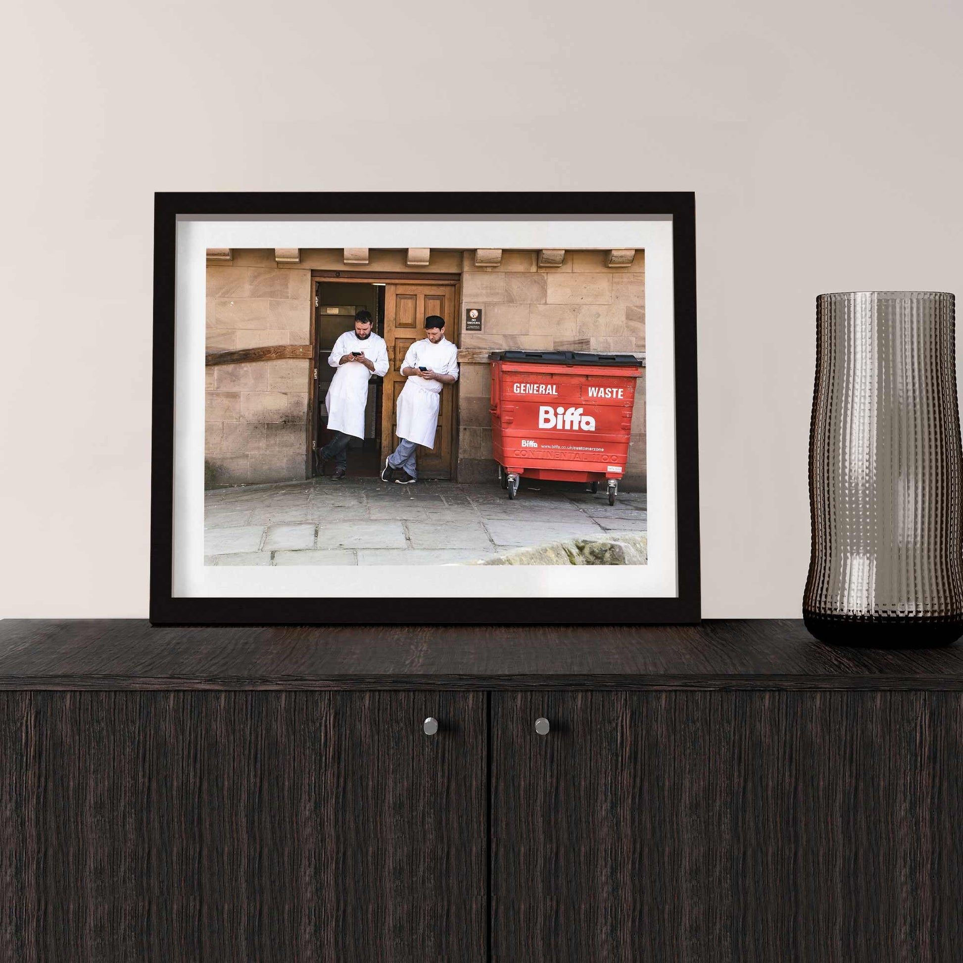 A photographic print was taken in Manchester, England showing street photography of two men on a break who stood by a wall.