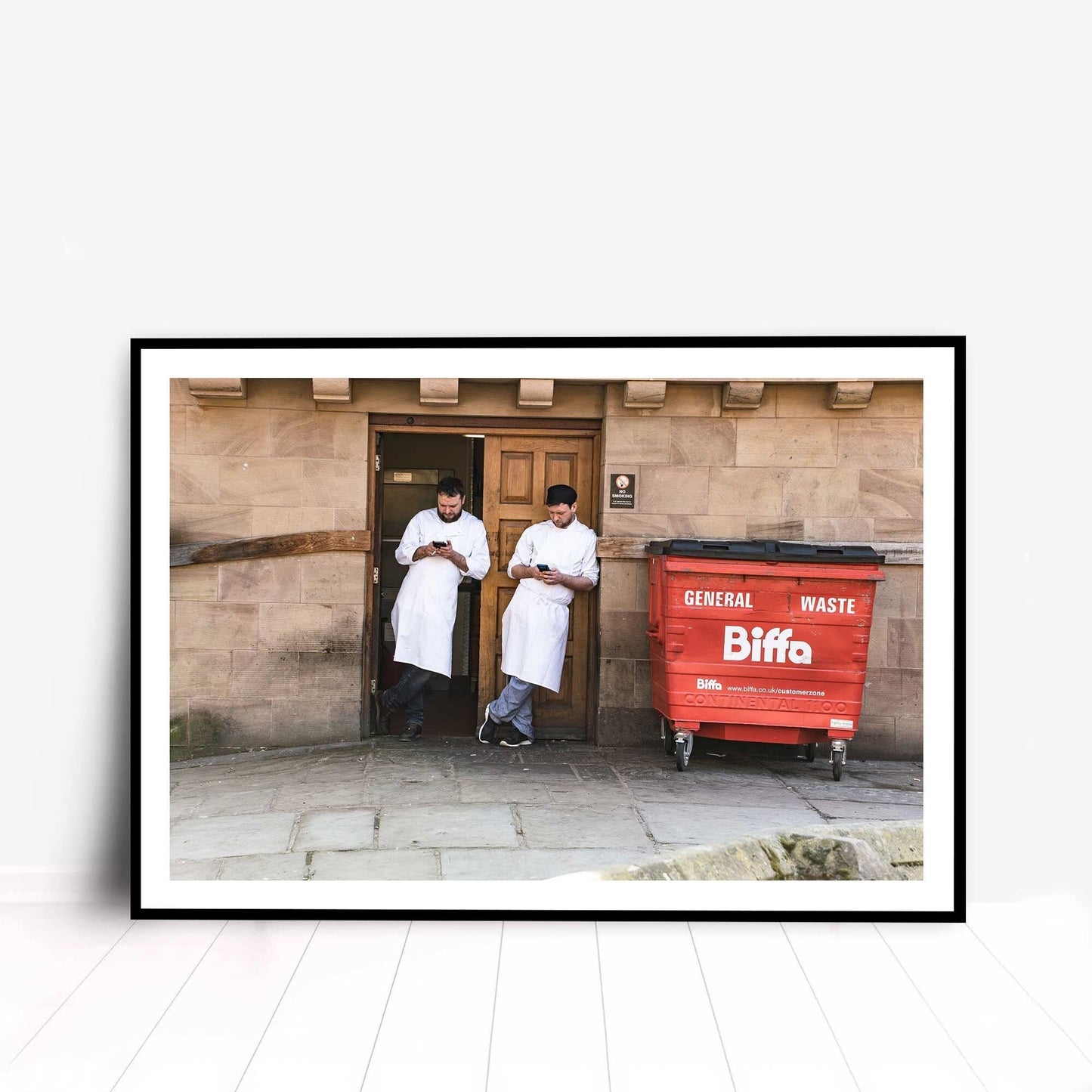 A photographic print was taken in Manchester, England showing street photography of two men on a break who stood by a wall.