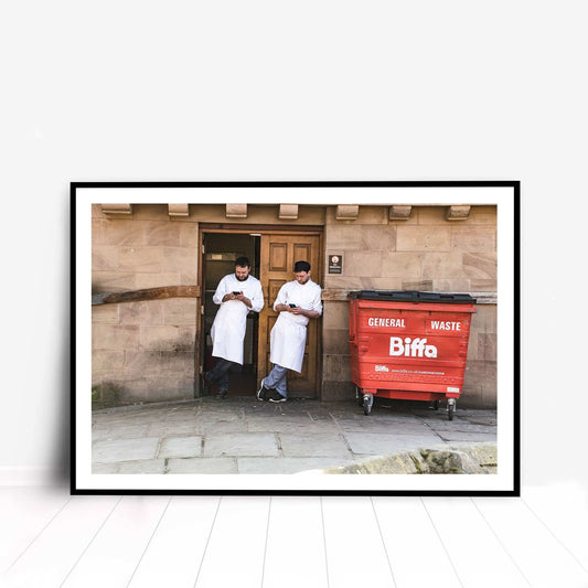 A photographic print was taken in Manchester, England showing street photography of two men on a break who stood by a wall.